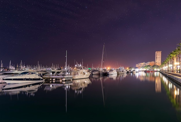 Marinehaven in Alicante bij nacht met luxejachten, schepen en vissersboten staan in rijen in de haven