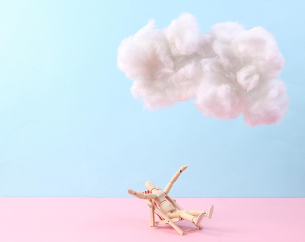 Marionet zonnebaden op ligstoel met wolk op pastel roze blauwe achtergrond Creatief idee Zomer strand rust Minimaal concept Pastelkleur trend