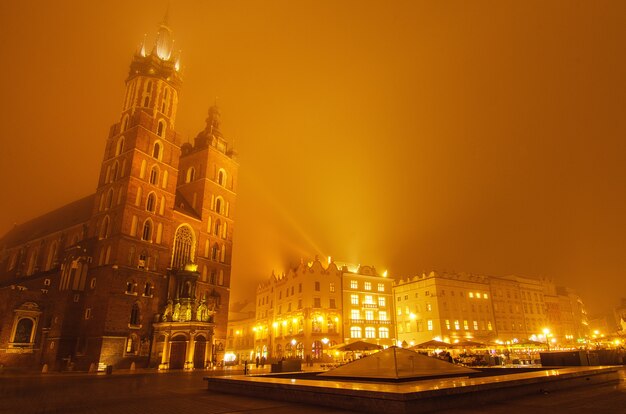 Market square in Cracow at misty night with St. Mary's Basilica with golden sky