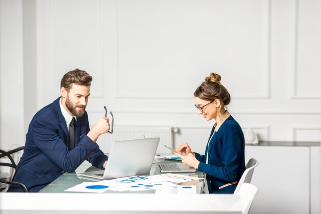 Marketeer of analyc-managerteam gekleed in pakken werkend met papieren kaarten en laptops in het witte kantoorinterieur