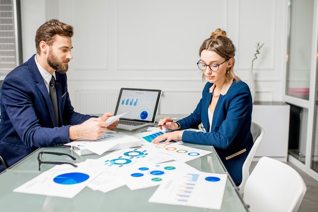 Marketeer of analyc-managerteam gekleed in pakken werkend met papieren kaarten en laptops in het witte kantoorinterieur