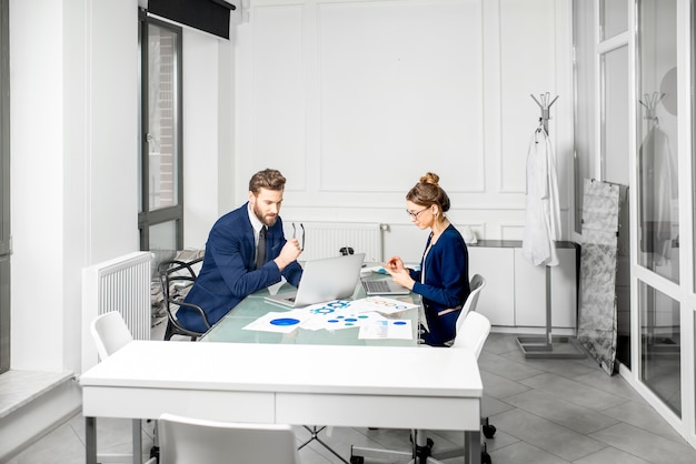 Marketer or analityc manager team dressed in suits working with paper charts and laptops at the white office interior