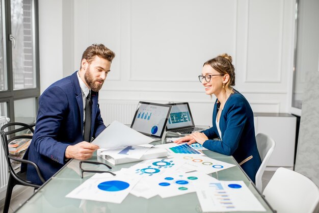 Photo marketer or analityc manager team dressed in suits working with paper charts and laptops at the white office interior