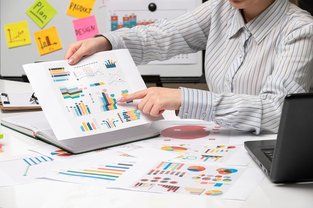 Marketing business lady in striped shirt in office with computer pointing at many graphs