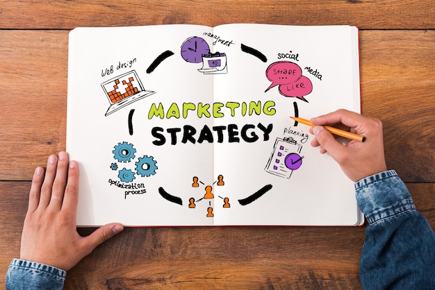 Photo marketing strategy. top view close-up image of man holding hands on his notebook with colorful sketches while sitting at the wooden desk