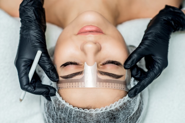 Markup with ruler on eyebrows of yong woman during permanent make up.