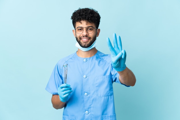 Marokkaanse tandarts man met tools geïsoleerd op blauw blij en drie tellen met vingers