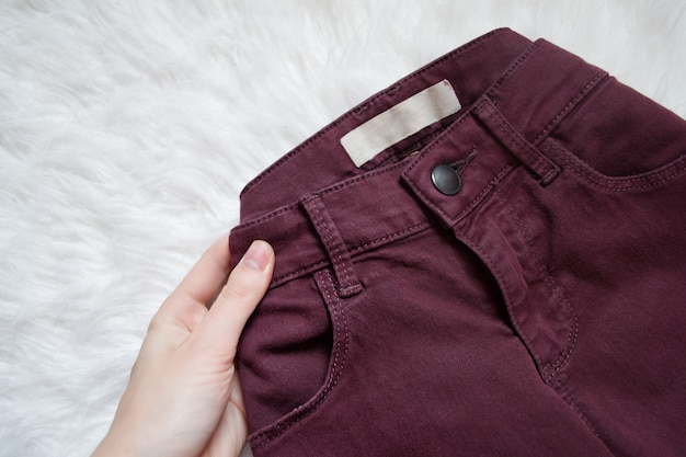 Maroon jeans in a female hand. Detail. Fashionable 
