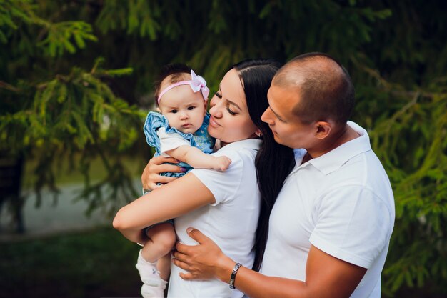 Married couple are holding child. against background trees