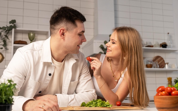 Foto coppia sposata cucinare a casa bella donna che alimenta il marito pomodoro mentre si fa insalata di verdure marito e moglie felici che si guardano l'un l'altro sorridendo e ridendo