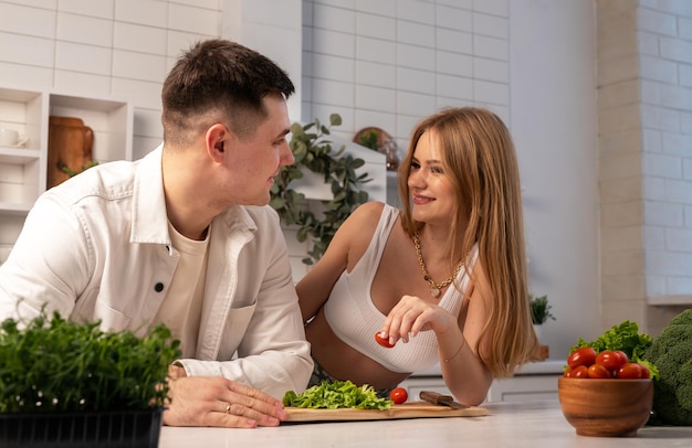 Супружеская пара готовит дома Красивая женщина и красивый мужчина готовят овощной салат улыбаясь смеясь Концепция счастливой семейной жизни