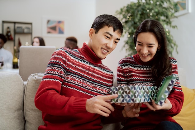 Married couple dressed in the same sweaters during christmas eve dinner is sitting on couch