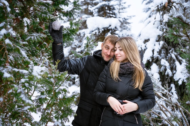 Married couple in an embrace hang christmas ball on christmas tree in snowy forest joyful mood from ...