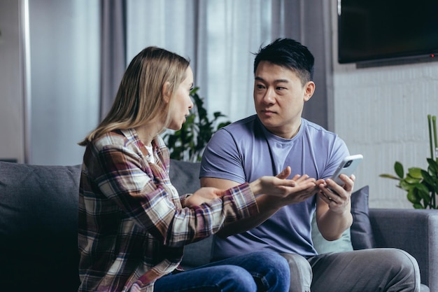 Married couple man and woman sitting on the couch at home and arguing over the phone jealousy