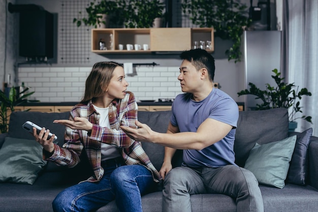 Married couple man and woman sitting on the couch at home and arguing over the phone jealousy