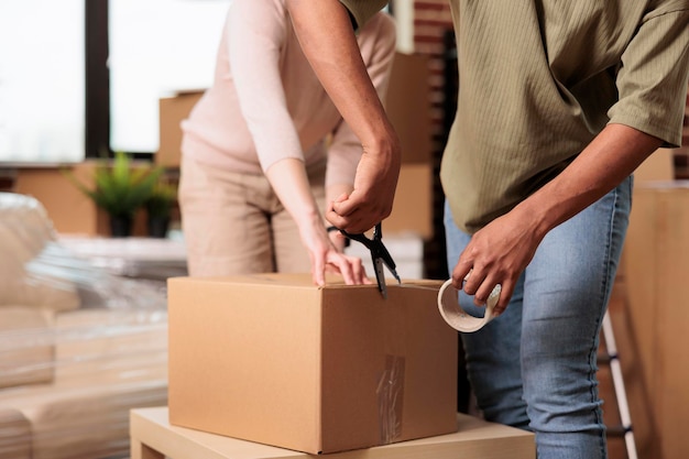 Married couple packing furniture in boxes with adhesive tape
roller, moving in new house bought on mortgage loan. using sticky
scotch to transport cargo storage in real estate property. close
up.