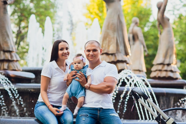 A married couple sitting on the edge of a city fountain, a child in his arms, concept of love