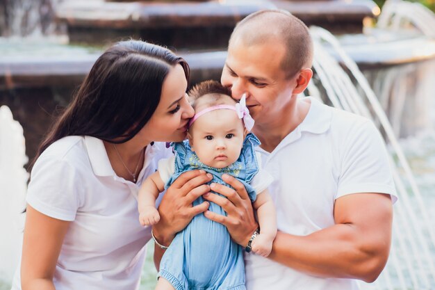 a married couple sitting on the edge of a city fountain, a child in his arms, concept of love