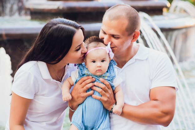 市の噴水の端に座っている結婚されていたカップル、彼の腕の中で子供、愛の概念