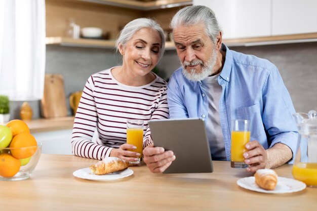 一緒にキッチンで朝食をとりながらデジタル タブレットを使用して老夫婦を結婚