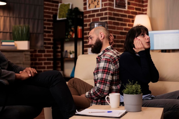 Married people fighting at couple therapy session with counselor, sitting back toback to talk about problems. Therapist giving advice, trying to solve relationship issues between partners.