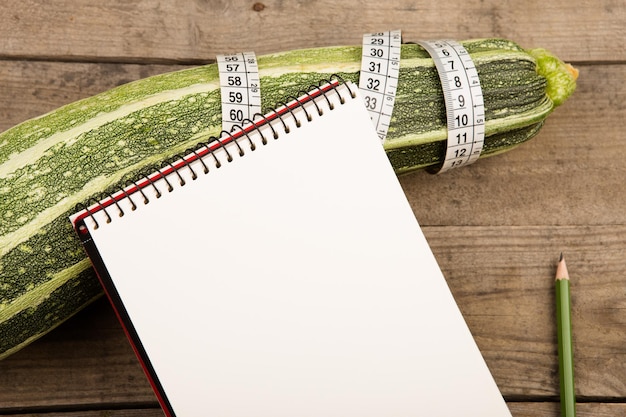 Marrow squash measure tape and blank notepad on brown wooden table