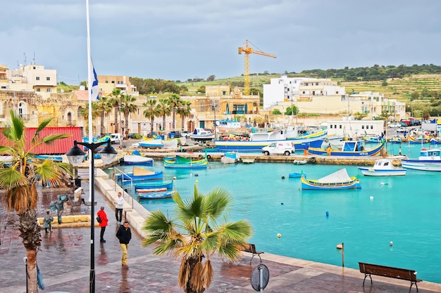 Marsaxlokk, Malta - 5 april 2014: Mensen en kleurrijke boten van Luzzu in de haven van Marsaxlokk, het eiland Malta