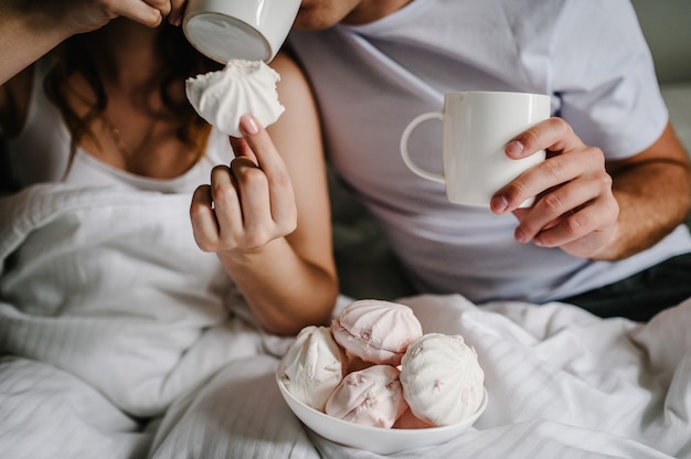 Marshmallow in mano sullo sfondo un uomo e una donna bevono caffè a letto