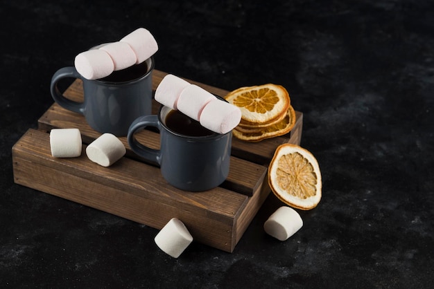 Marshmallow met koffie in kopje met gedroogde gesneden sinaasappel op snijhouten plaat