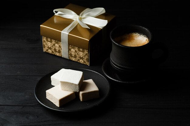 Marshmallow op een zwarte lijst met gouden giftdoos en coffekop