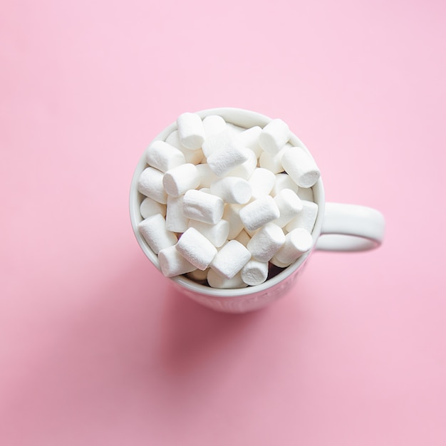 Marshmallow poured from a white mug on a pastel pink