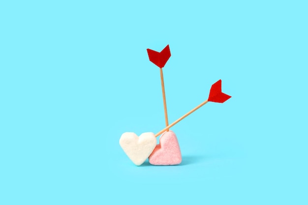 Marshmallow in the shape of a heart with arrows on a blue background. A cute interpretation of love and Valentine's Day.