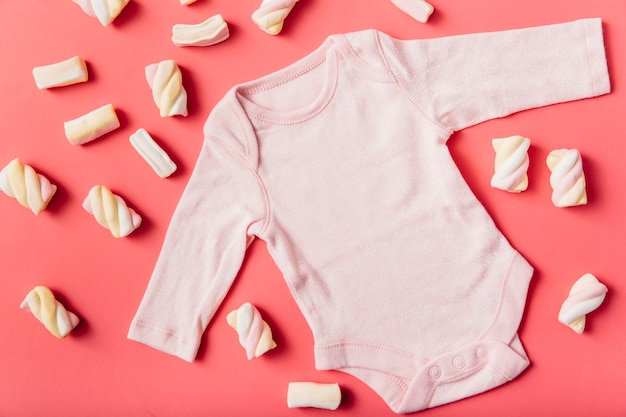 Photo marshmallow surrounded with pink baby onesie on peach background