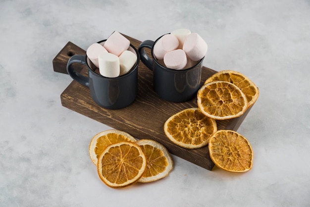 Marshmallow con caffè in tazza con arancia affettata secca sul piatto di legno di taglio