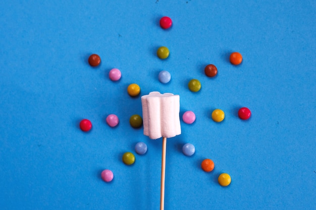 Marshmallows composition on wooden skewers on a blue background. flat lay, holiday concept. sun-shaped sweets