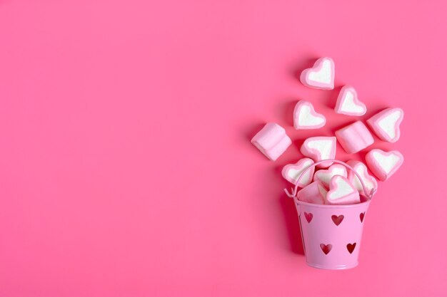 marshmallows heart shaped spilled from pink iron bucketon pink background Happy Valentine's Day