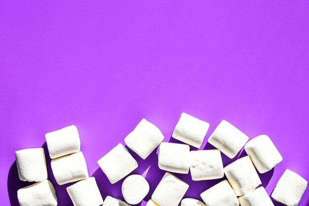 Marshmallows on purple background with copy space. flat lay. top view. background or texture of colorful mini marshmallows. winter food background concept. junk unheathy food