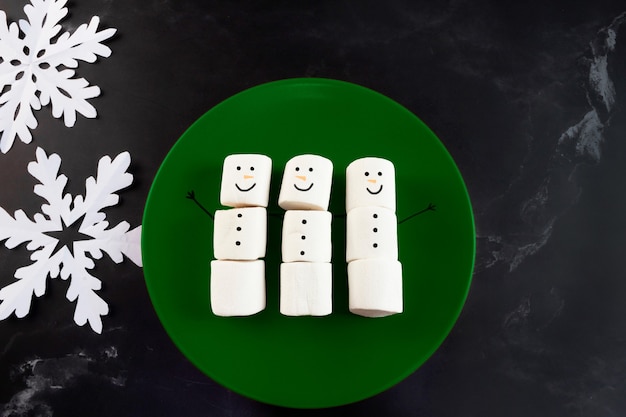 Marshmallows snowman on green plate and snowflakes on the side