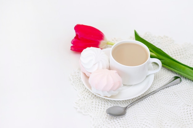 marshmallows, tea or coffee with milk and a tulip flower. on a light surface romantic spring morning. delicate breakfast, breakfast in bed. for the beloved. surprise.