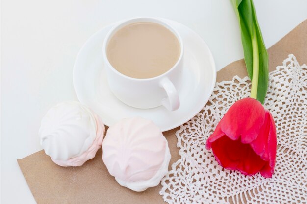 marshmallows, tea or coffee with milk and a tulip flower. on a light surface romantic spring morning. delicate breakfast, breakfast in bed. for the beloved. surprise.