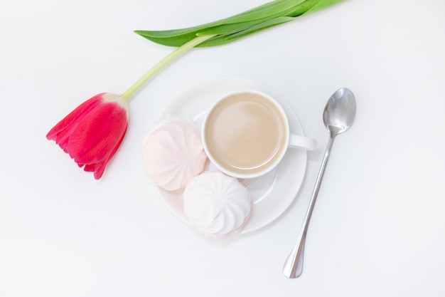 Marshmallows, thee of koffie met melk en een tulpenbloem. op een lichte ondergrond Romantische lentemorgen. delicaat ontbijt, ontbijt op bed. voor de geliefde. Verrassing.