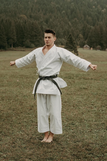 Arte marziale del karate un uomo in kimono con cintura nera si allena sullo spazio libero della montagna