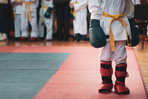 Martial art The kid at the competitions in kimano with a yellow belt and big blue boxing gloves to prepare for the fight For atmospheric added film noise effect