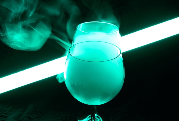 Martini cocktail covered with a smoke in a neon green light. Illuminating tube is glowing