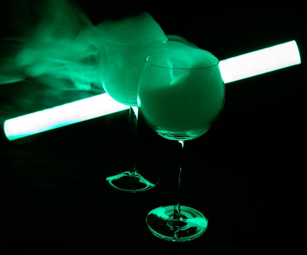 ネオン グリーンの光の中で煙で覆われたマティーニ カクテル。照明管が光っている