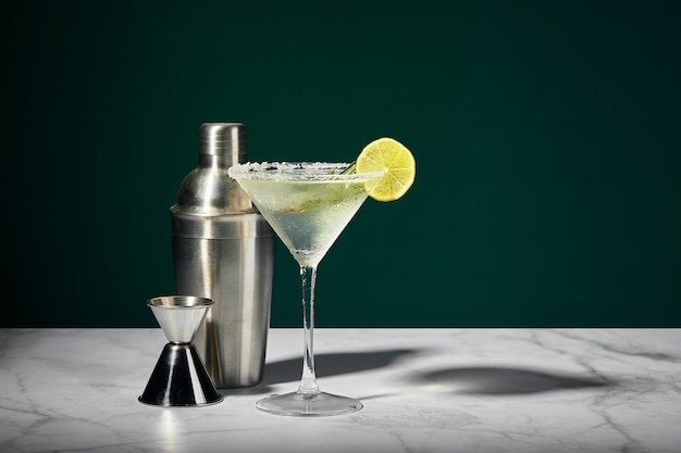 Martini glass with cocktail or mocktail and lime wedge shaker and jigger on dark background