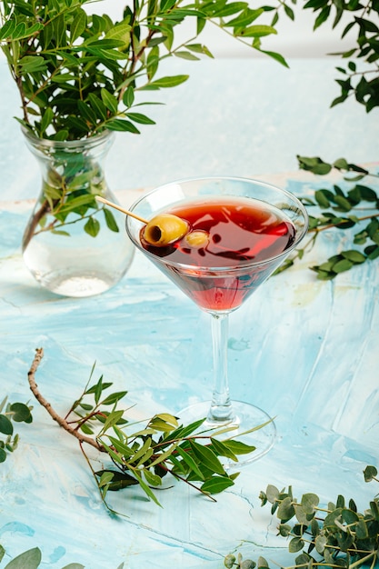 Martini glass with red alcohol cocktail and green olives