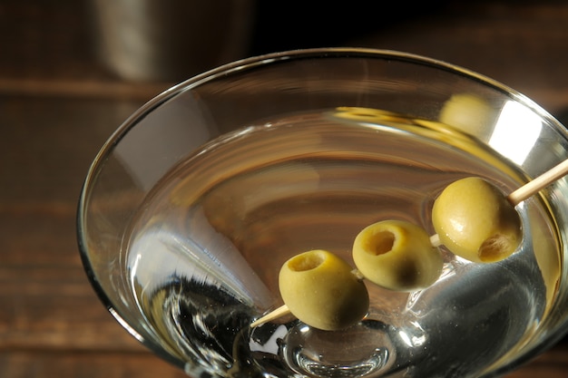 Martini in een glas wijnglas met groene olijven op een spies op een bruin houten tafel. cocktails. bar