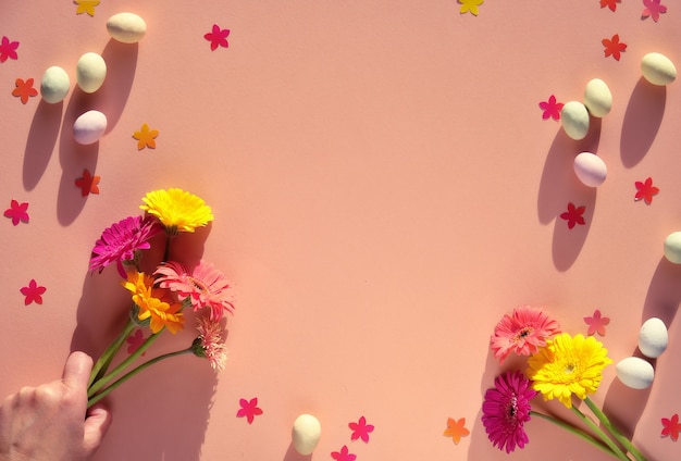 Marzipan Easter eggs, gerbera flowers and confetti on orange paper.