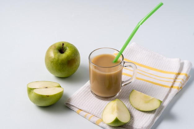 Masala chai tea in a glass cup and fresh apples over white table.